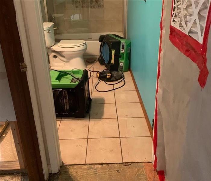 SERVPRO dehumidifier and air scrubber near power tools in a bathroom with at least some removed drywall, partially removed wo